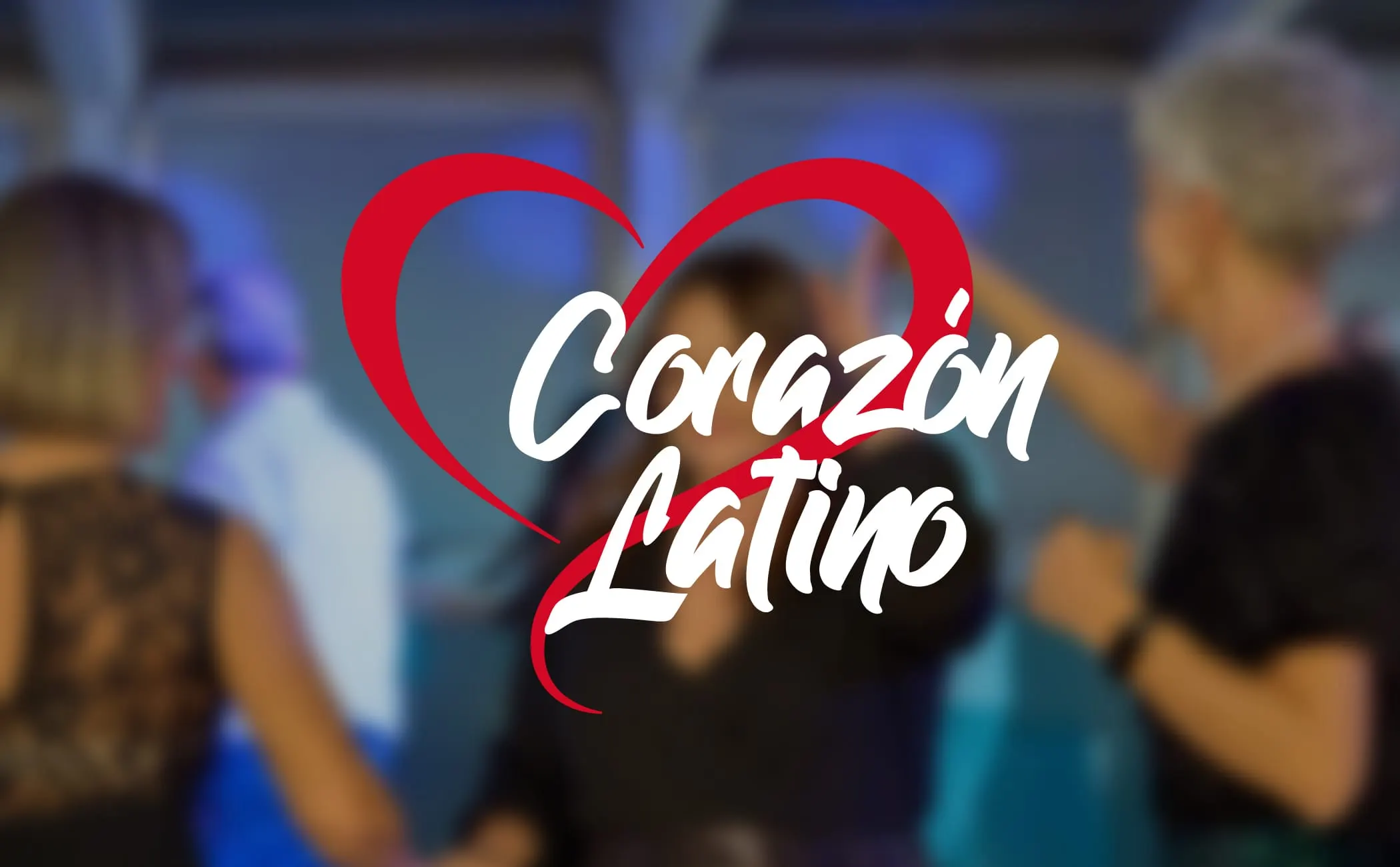 Il logo Corazon Latino, cuore rosso e lettering bianco, su una sala da ballo sfocata